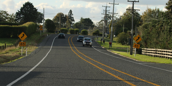 Two yellow lines are in the middle of the road create a wide centre line, with cars driving on either side of the lines