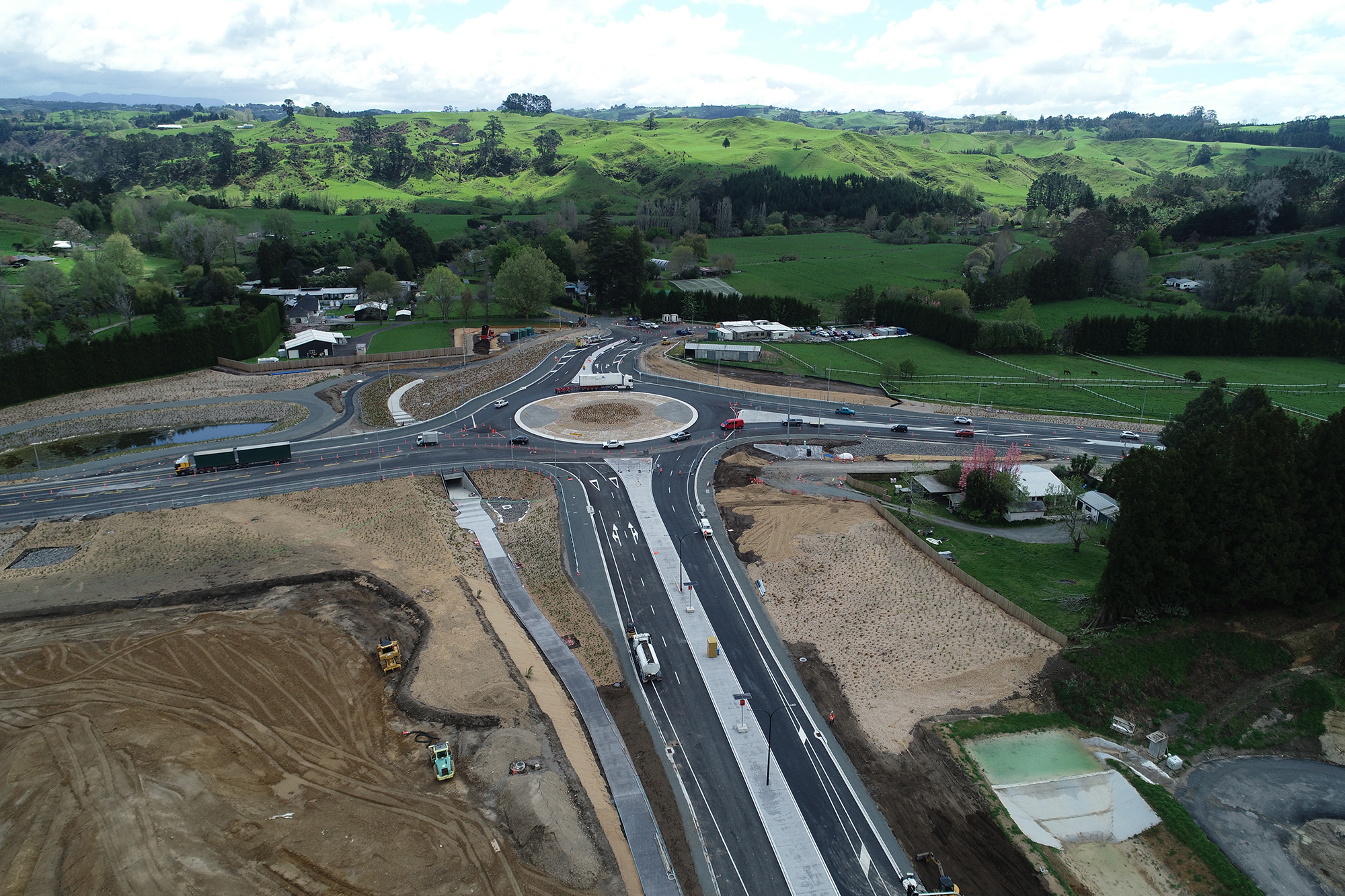 Aerial view of roundabout with traffic with surrounding landscape under construction.